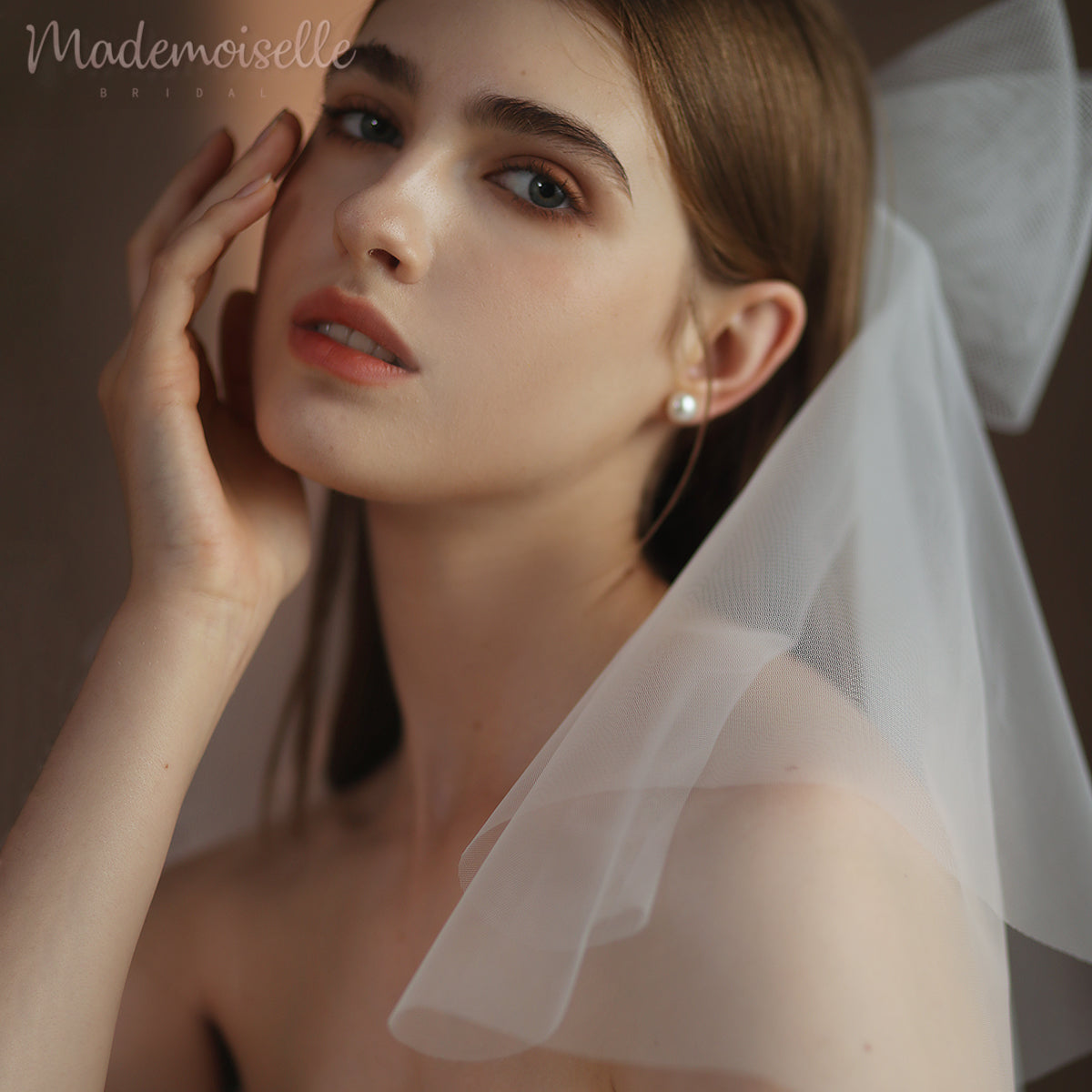 A graceful woman in a delicate veil, gently touching her face, exuding elegance and mystery.