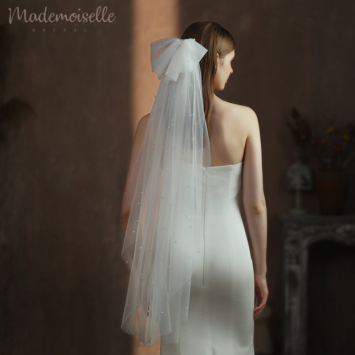 The back view of a bride adorned in a delicate white pearl wedding veil with an oversized bow, embodying timeless beauty and romantic allure.