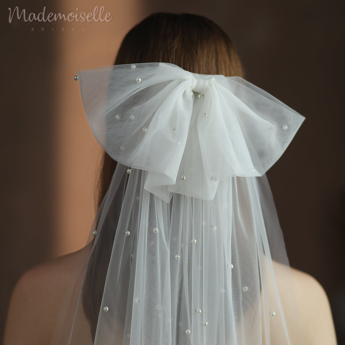 A bride's elegant pearl veil with an oversized bow drapes gracefully over the back of her head, adding a touch of sophistication to her bridal look.