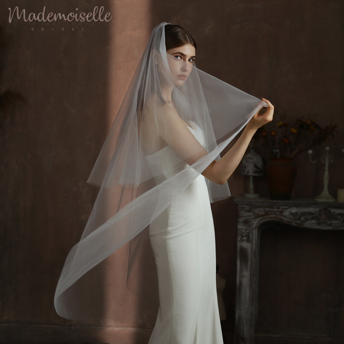 With a delicate touch, the bride elevates her veil, showcasing her exquisite style and the joy of her wedding day.