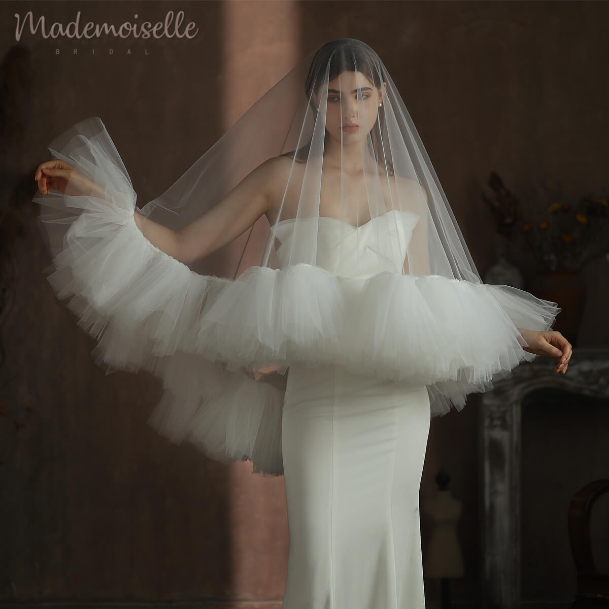 The bride, draped in a white wedding dress, showcases a delicate tulle veil with ruffle edges, epitomising bridal beauty.