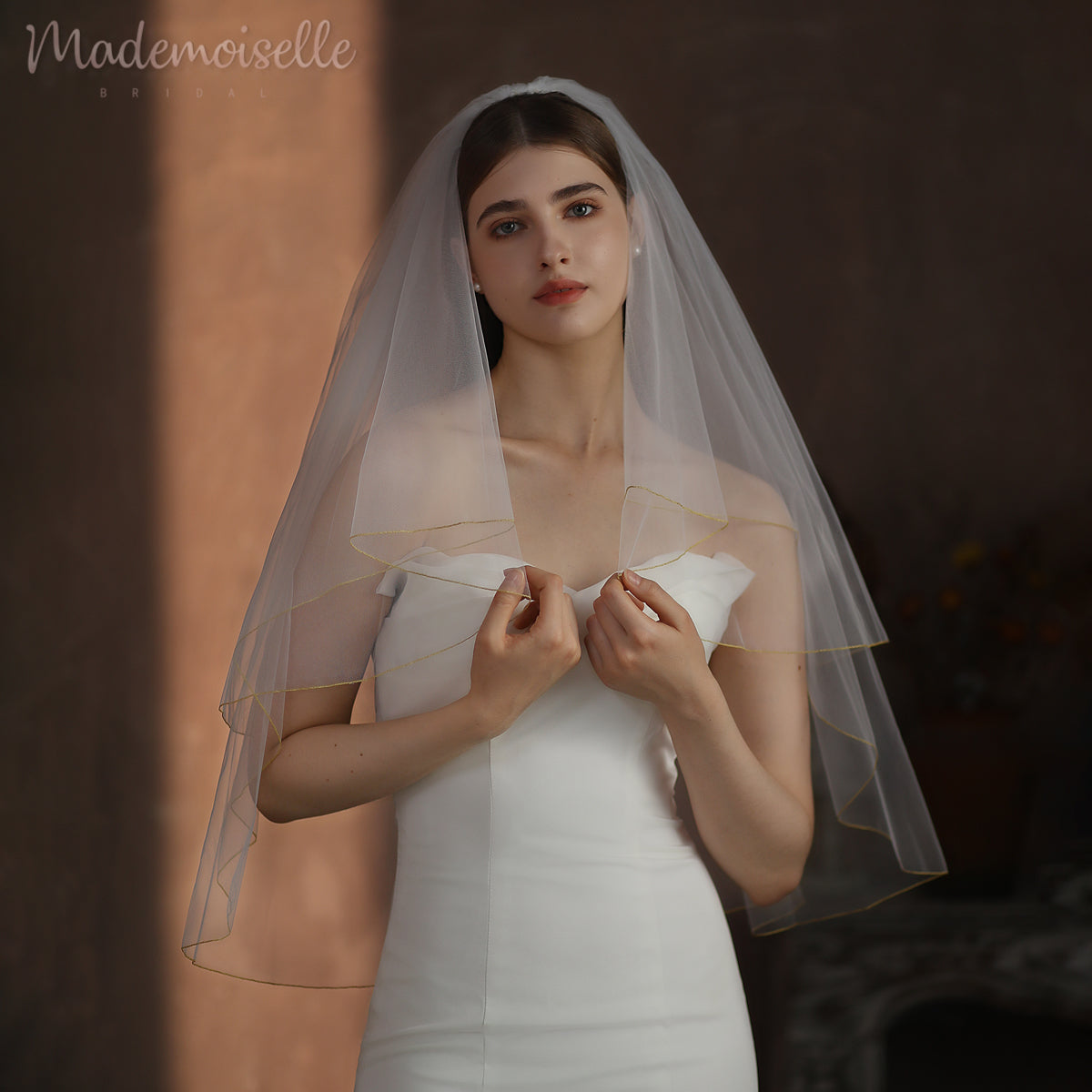 A beautiful woman in a white wedding dress, complemented by a flowing veil with golden threaded trim, embodies timeless bridal elegance.