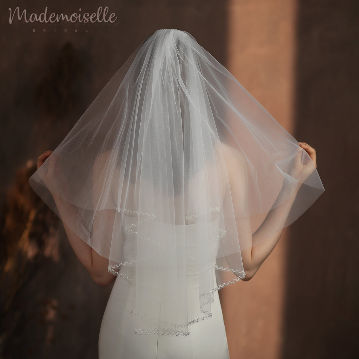 A bride's silhouette from behind, showcasing a luxurious veil with a beaded edge, radiating sophistication and charm.