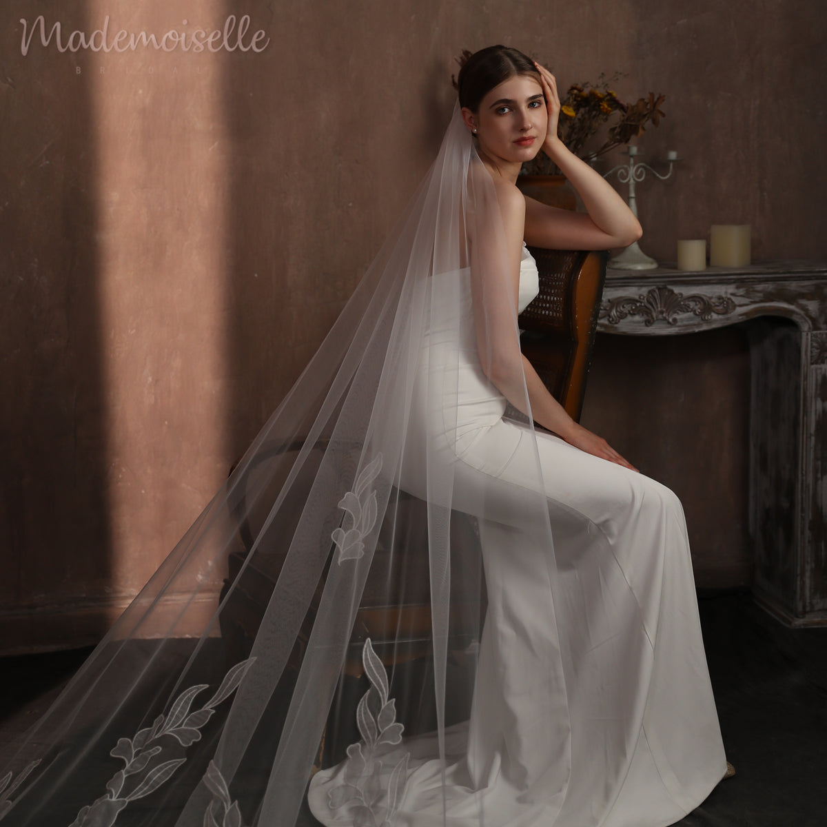 A bride in a floral lace wedding veil gracefully seated on an elegant chair, exuding timeless beauty and romance.