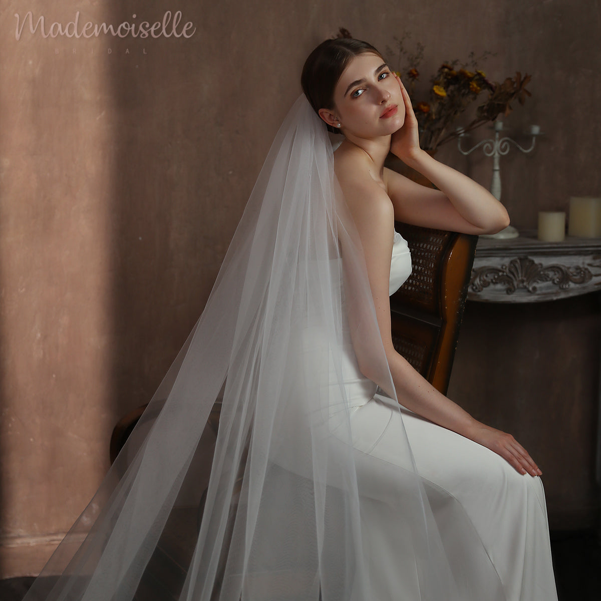 A beautiful bride in a wedding gown, featuring a cathedral veil, seated gracefully on an exquisite chair.