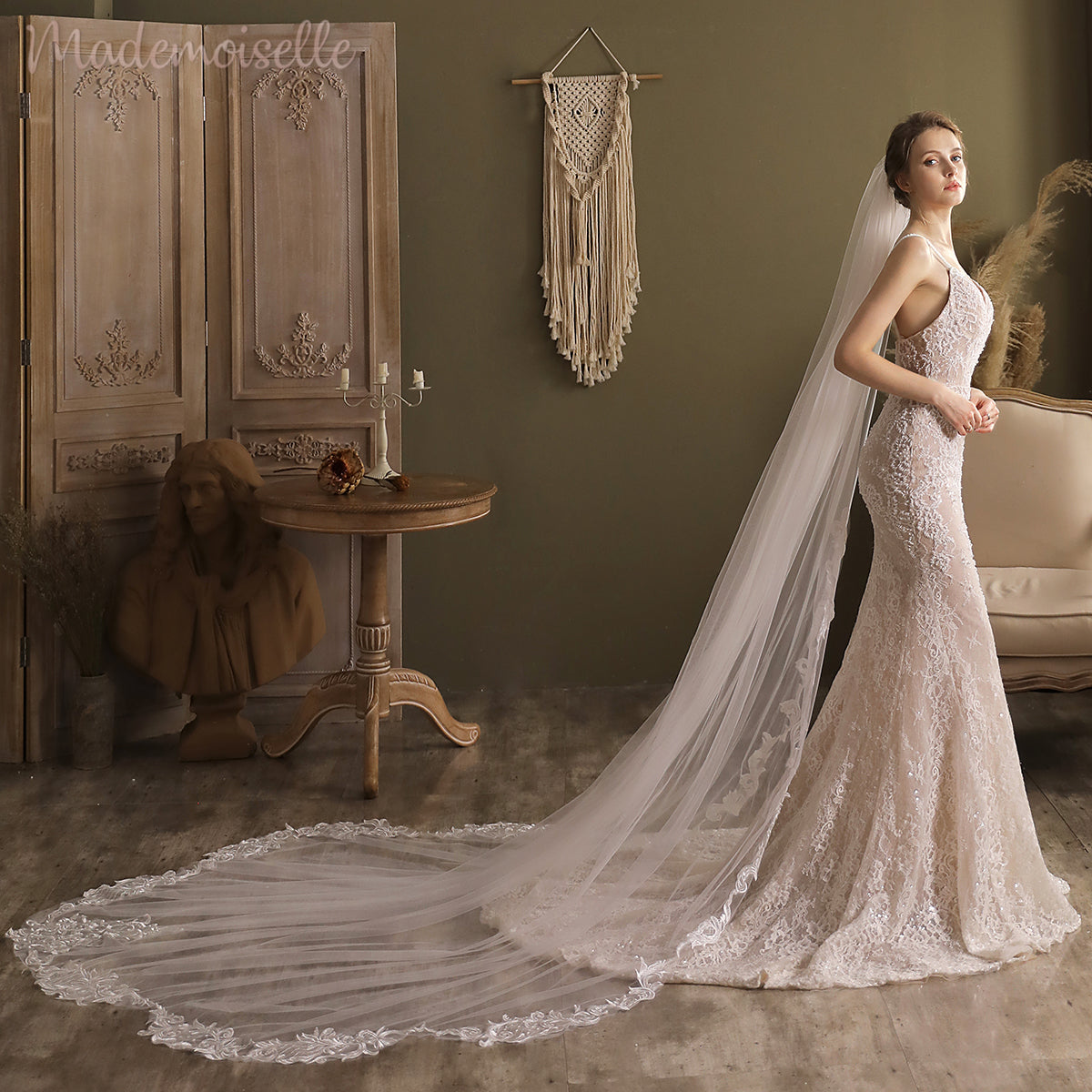 A beautiful woman in a lace appliqué wedding veil poses elegantly in a luxurious room, embodying grace and romance.