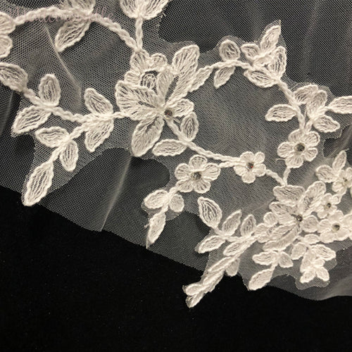 An exquisite close-up of a wedding veil featuring intricate lace appliqué edges and charming white flowers, radiating elegance.