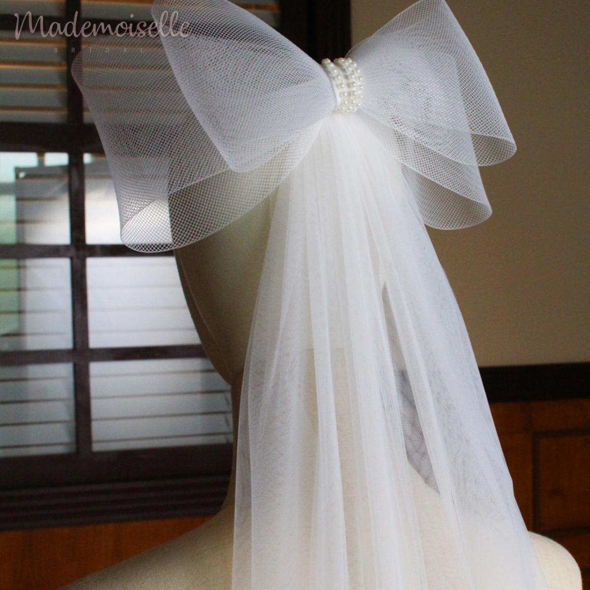 A stunning white wedding veil embellished with a lovely bow and pearl beads, capturing the essence of elegance for a memorable wedding day.