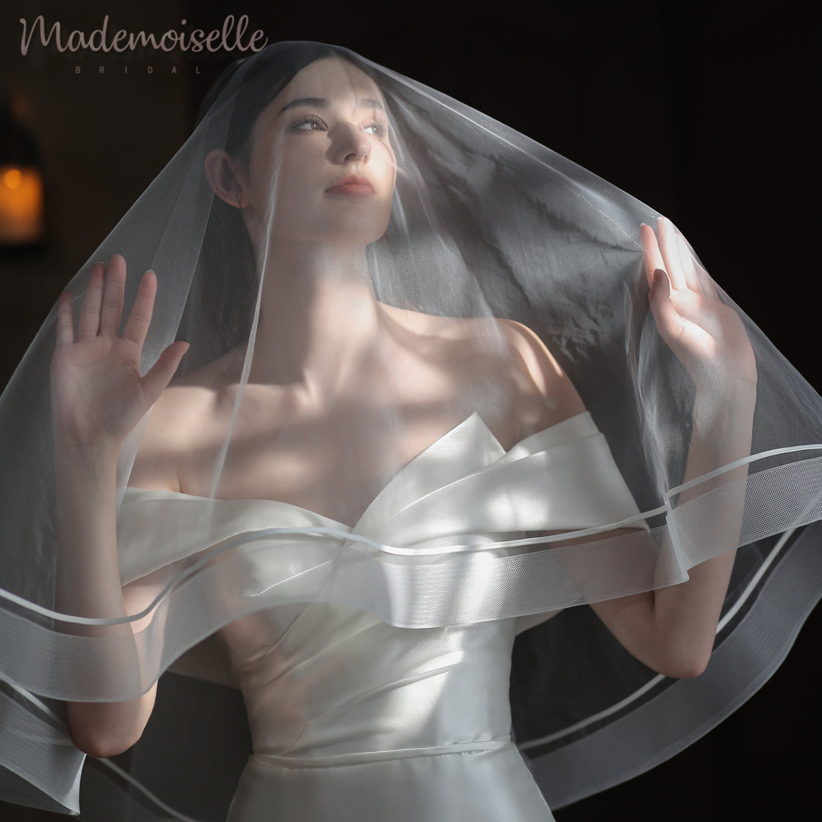 A bride in a stunning wedding dress delicately holds her veil adorned with exquisite horsehair trim.