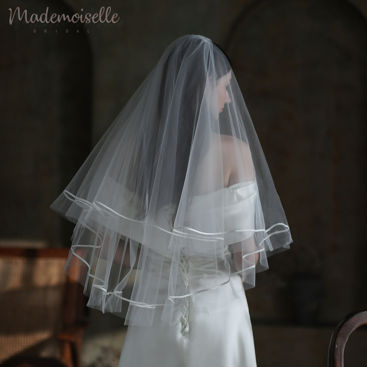 A bride in a stunning white wedding dress, gracefully adorned with a delicate veil with elegant ribbon trim