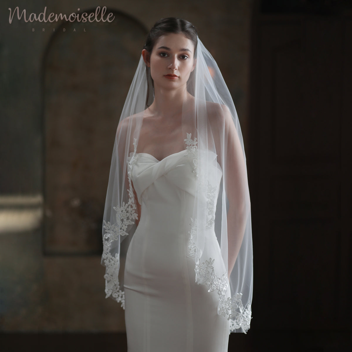 Dressed in an exquisite white wedding gown, the bride&#39;s beautiful veil with lace edge cascades elegantly, highlighting her enchanting presence on this special day.