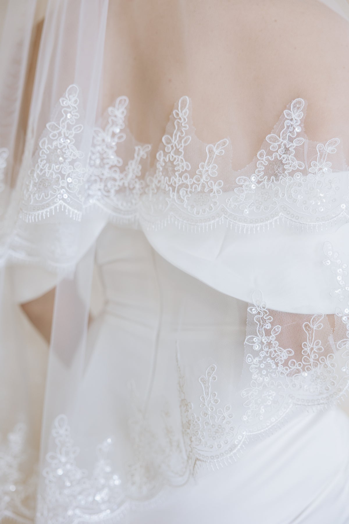 Close-up of a white bridal dress with intricate floral lace applique and a matching sheer veil draped over the shoulders.