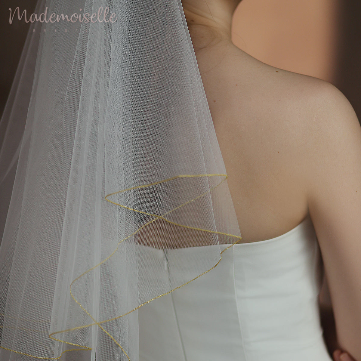 A radiant bride in a stunning wedding dress adorned with golden threaded trim, gracefully wearing a delicate veil.