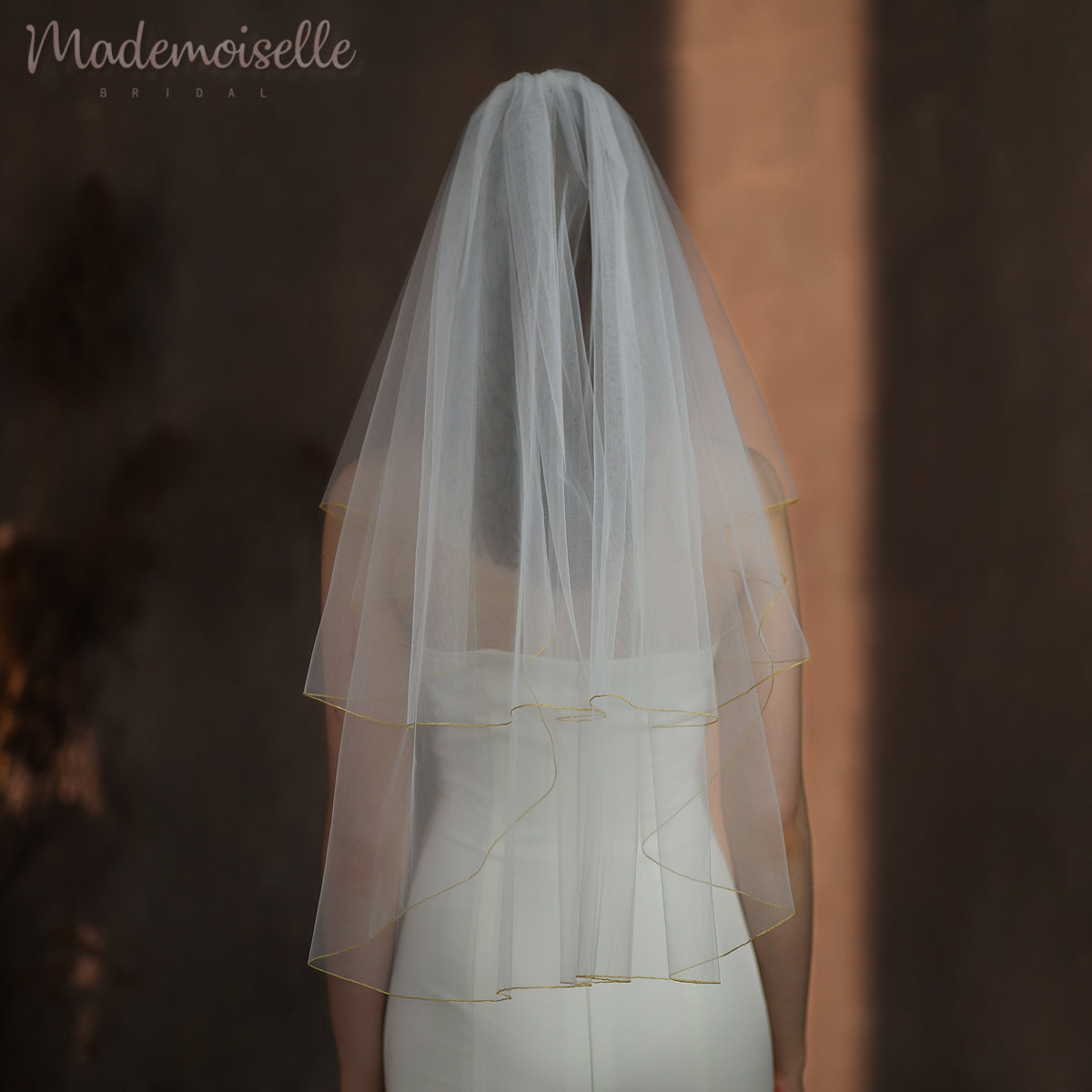 A radiant bride in a stunning wedding dress adorned with golden threaded trim, gracefully wearing a delicate veil.