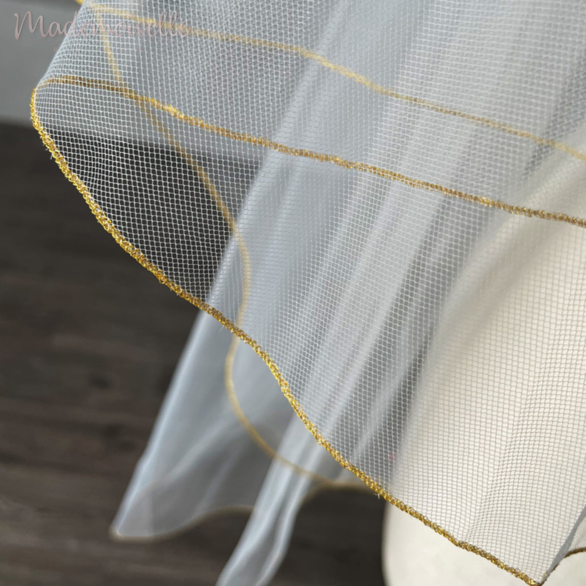 An elegant close-up of a white tulle veil with luxurious gold accents, featuring intricate golden threaded trim for a refined touch.
