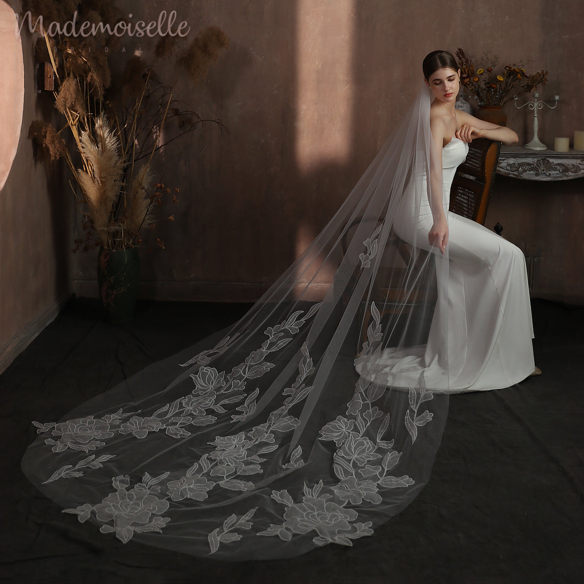 A bride adorned in a floral lace veil sits gracefully in an elegant room, radiating beauty and anticipation.