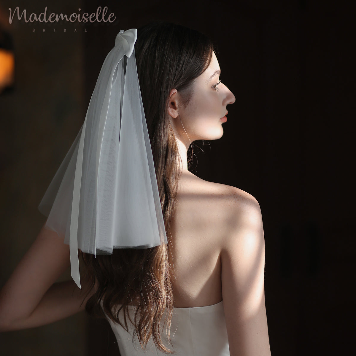 A bride in a luxurious wedding dress, complemented by a delicate veil with satin bow detail, embodies elegance and romance in her enchanting moment.