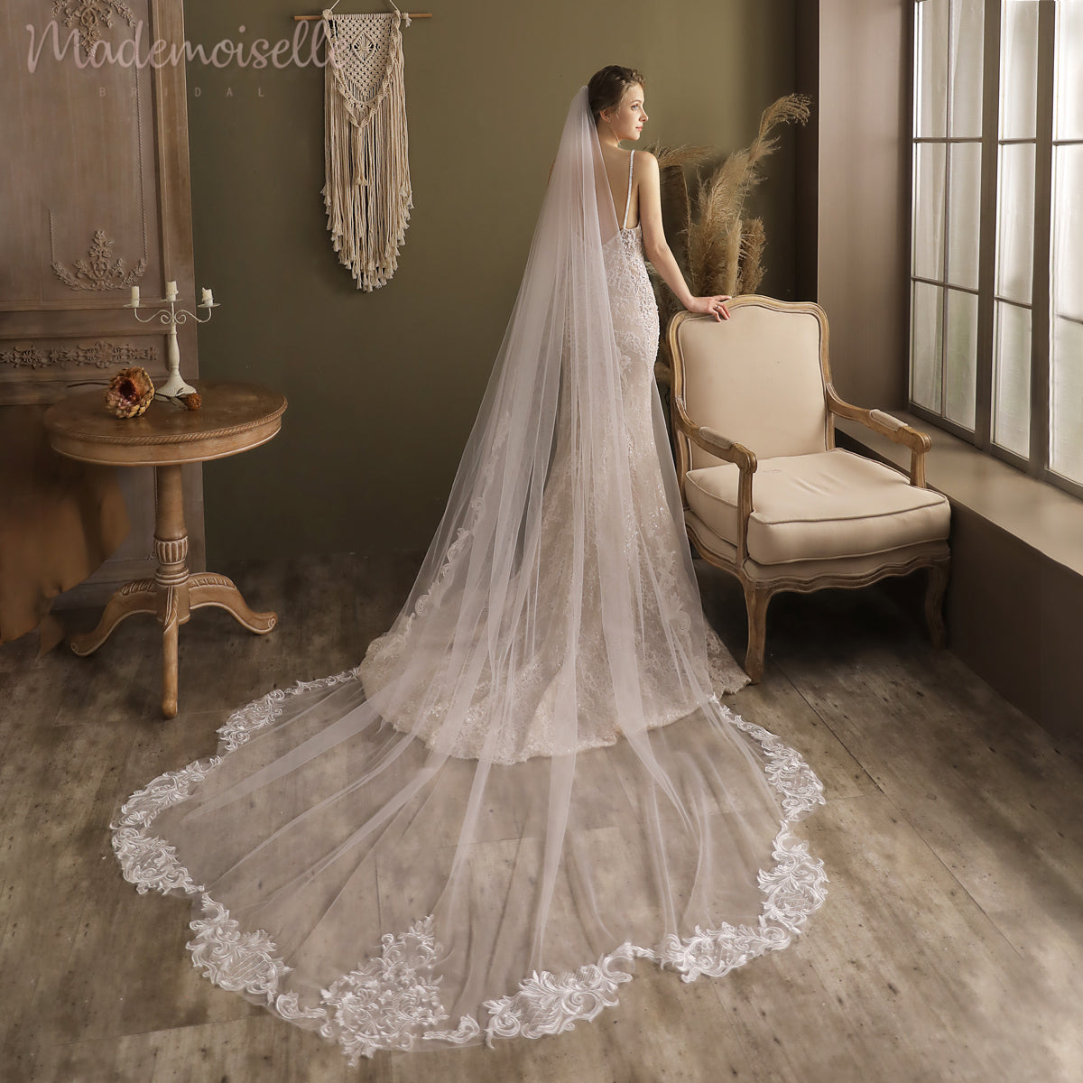 A beautiful bride in a sophisticated cathedral length wedding veil stands poised by a window, exuding elegance and bridal bliss.
