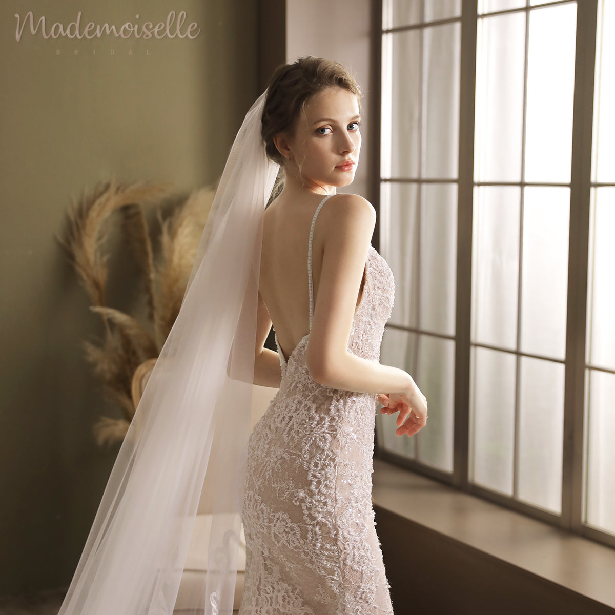 A woman in an exquisite wedding gown adorned stands poised by a window, embodying timeless beauty.