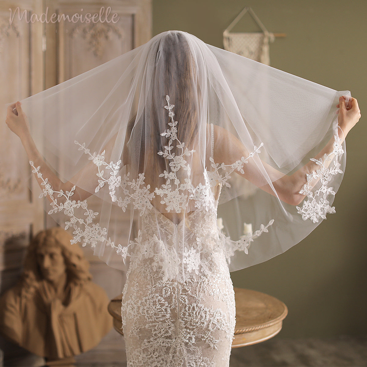 A bride adorned in a delicate lace veil, embellished with floral accents and a lace appliqué edge, radiates elegance.