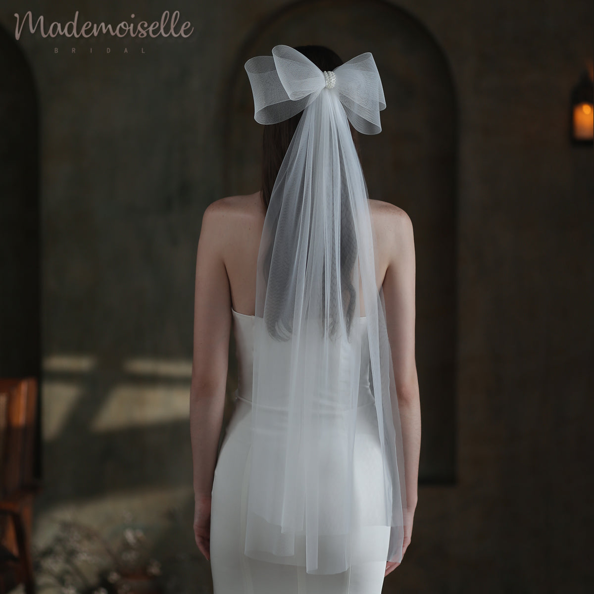 A bride&#39;s back, elegantly showcased with a flowing veil with an oversized bow and pearl beads details, embodying the enchanting allure of a wedding day.