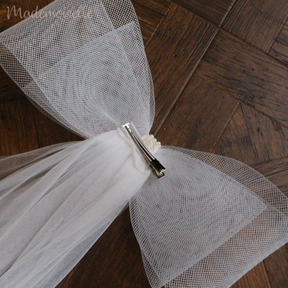 The back view of a stunning white veil elegantly topped with a charming bow and a silver hairpin for easy attachment on the bride&#39;s hair, embodying timeless beauty and charm.