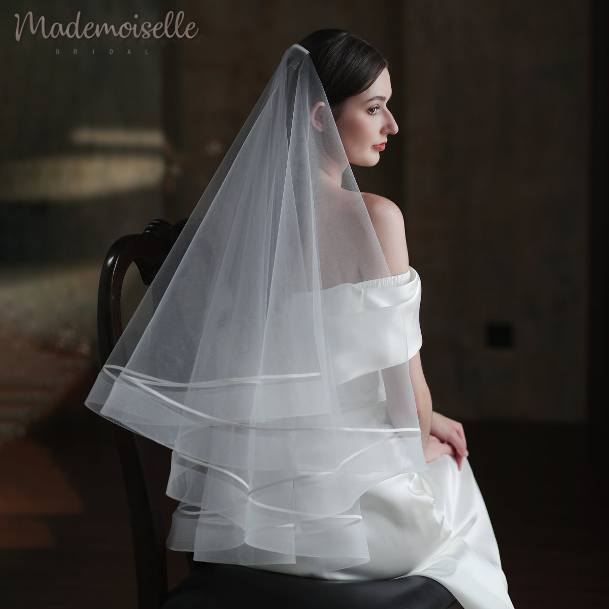 A stunning woman in a wedding veil featuring horsehair trim, elegantly perched on a chair, radiating bridal charm and sophistication.