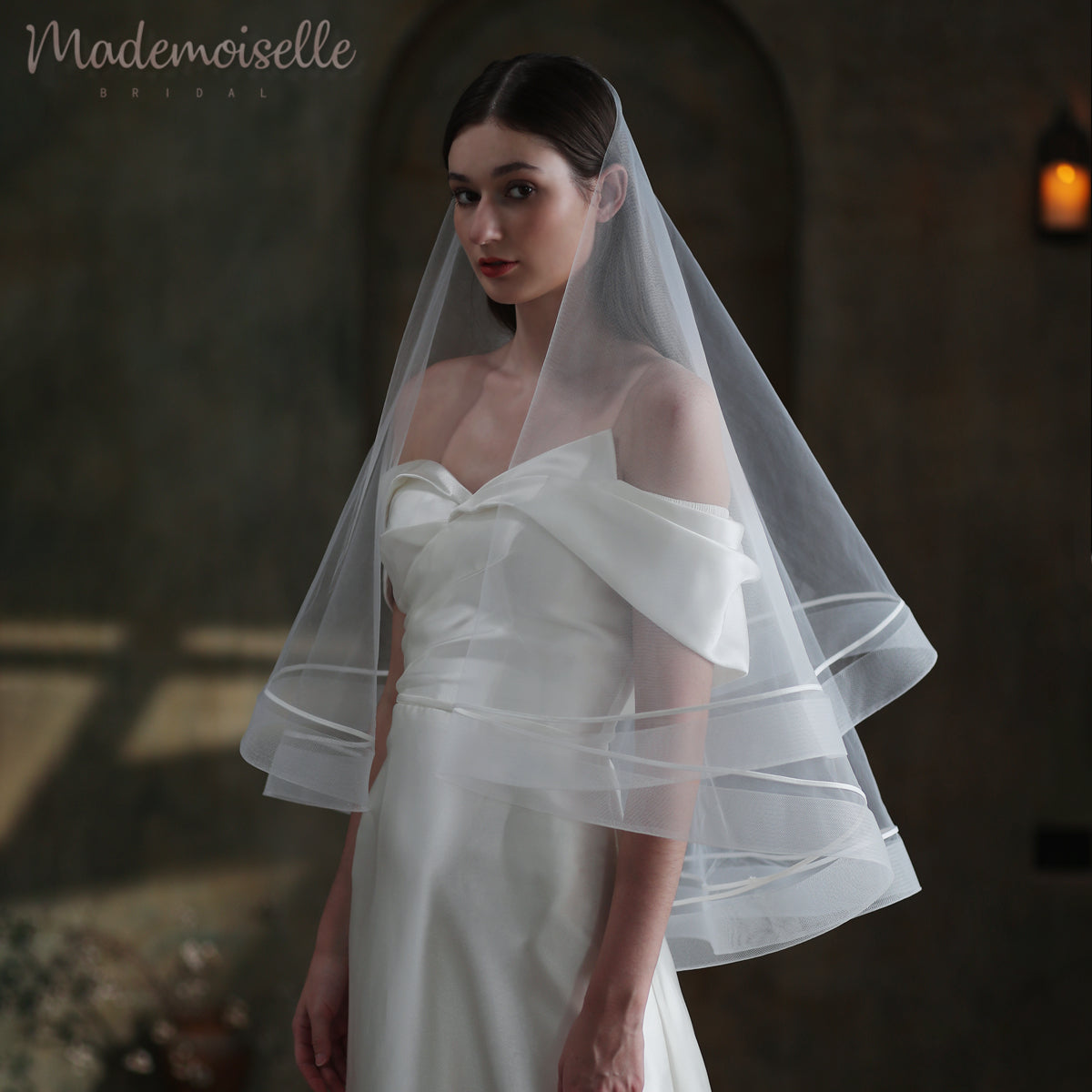 A bride adorned in a delicate white wedding veil, featuring elegant horsehair trim and a luxurious satin ribbon trim.