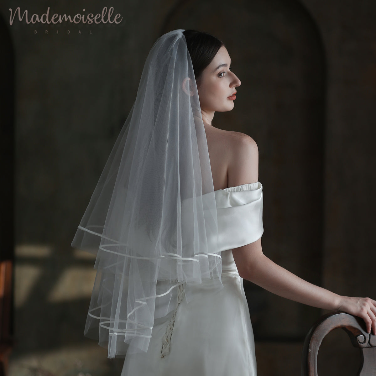 Dressed in a white wedding gown, the bride&#39;s veil with exquisite ribbon trim enhances her enchanting and timeless beauty.