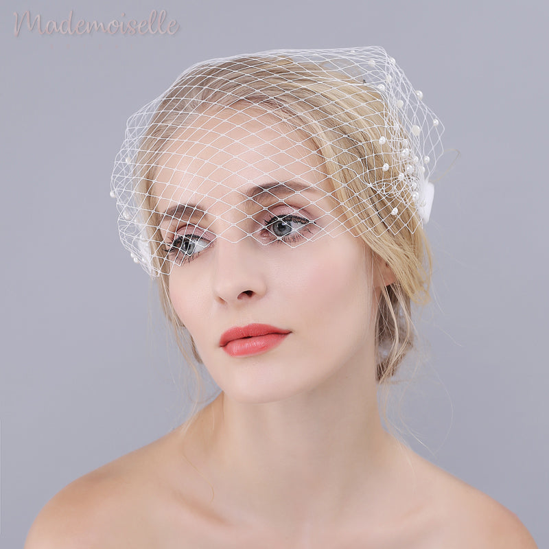 A front view of model wearing a white netted birdcage wedding veil with pearl beads